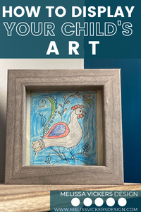 White and teal wall with a framed photo of a chicken drawn by a child.