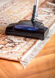 Blue and black vacuum on a neutral patterned rug on light wood floor.